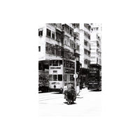 Black and white street scene featuring a person pushing a cart between two double-decker trams in a city.