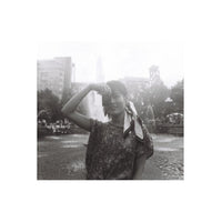 Person holding a small 110 camera in a park, captured in high-contrast black and white film with a grainy, vintage aesthetic.