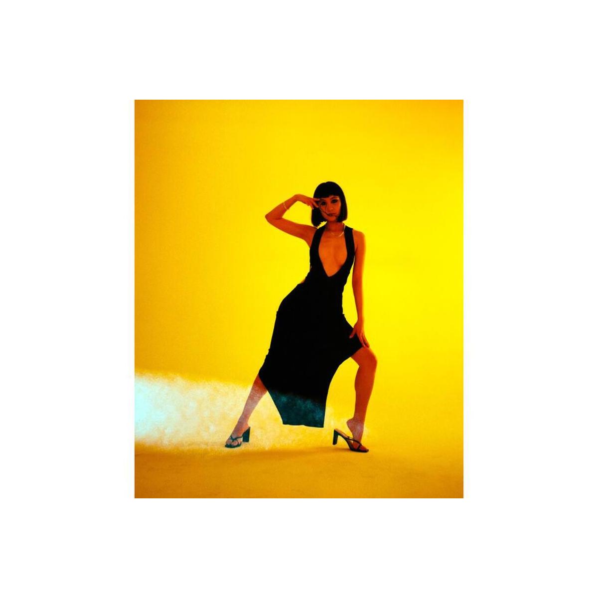Woman in a black dress posing against a vibrant yellow background, captured with Lomography Redscale 120 film effects.