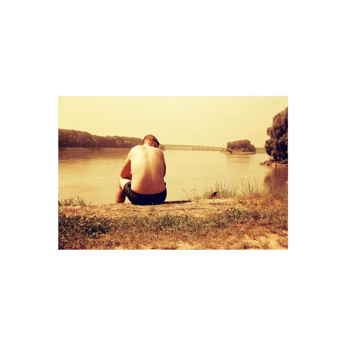 A person sits by a river in a landscape captured with Lomography Redscale film, featuring warm orange and yellow tones.