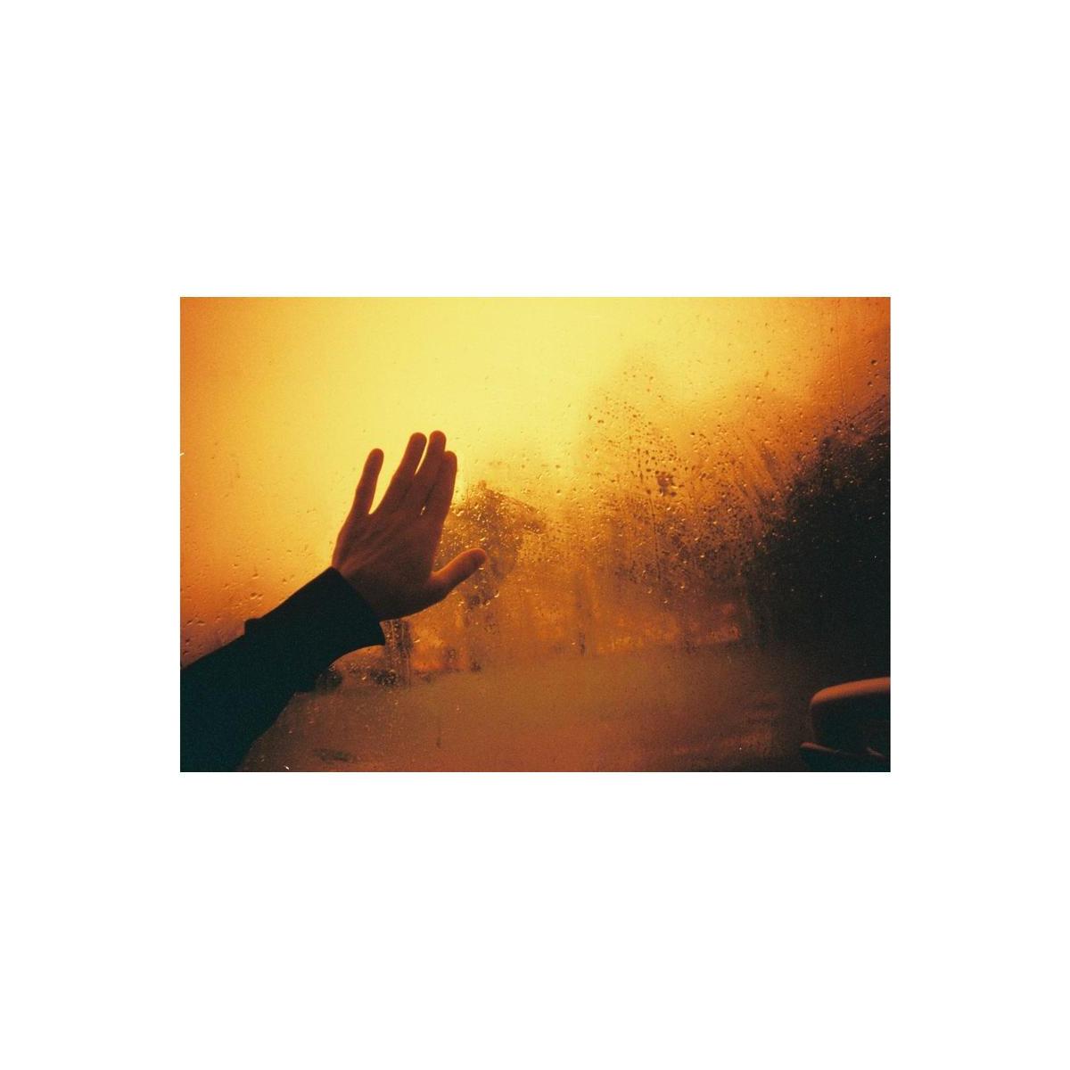 Hand reaching toward a rain-streaked window with warm, golden redscale film tones and high contrast.