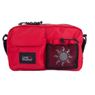 A red crossbody bag with a front pocket featuring a black 'Long Weekend' brand patch and a black mesh pocket with a sun design, shown on a white background.