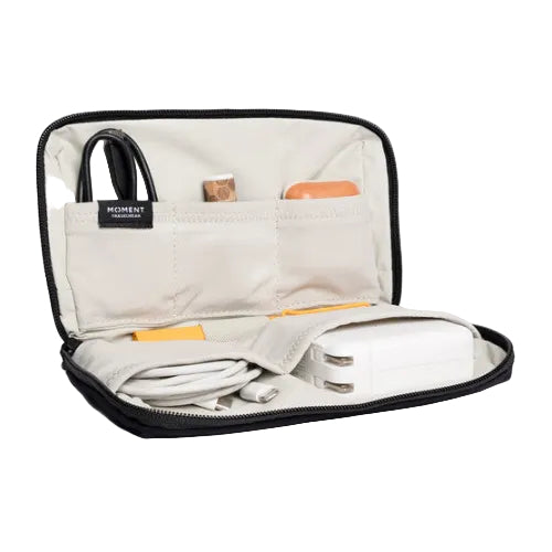 A gold-colored Moment Mini Tech Organizer with various items like cables and a charging device placed inside, showing the different compartments.