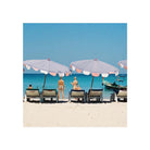 A square beach scene print showing white umbrellas over lounge chairs on a sandy shore, with turquoise water and a clear blue sky. Two people are visible near the umbrellas, and a small boat appears on the right.
