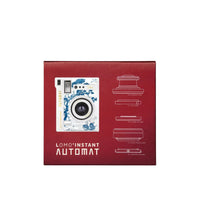 Red Lomo Instant Automat camera packaging box featuring a white and blue Japanese wave-patterned camera illustration, white technical line drawings, and the LOMO INSTANT AUTOMAT text on a light gray background.