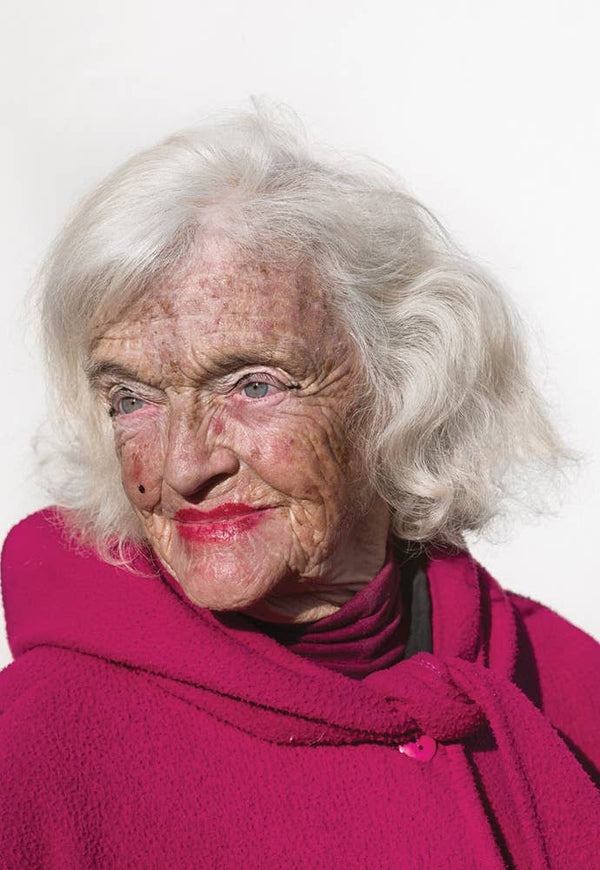 Woman with white hair wearing a pink coat against a white background