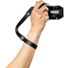 Hand holding a camera with a black strap on a white background