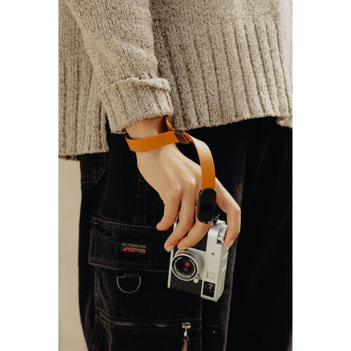 Person holding a camera with an orange strap against a neutral background