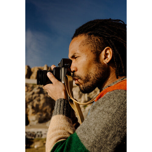 Man with dreadlocks holding a camera against a scenic background