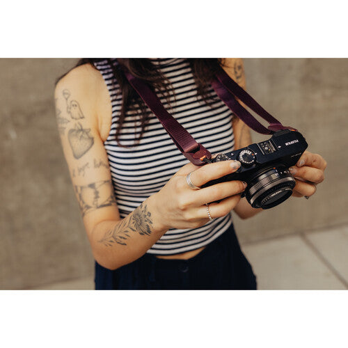 Person holding a camera with a strap, wearing a striped shirt against a neutral background
