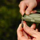 Person holding a green phone case with a lanyard attachment against a blurred natural background