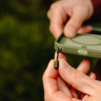 Person holding a green phone case with a lanyard attachment against a blurred natural background