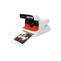 White and orange Polaroid Flip instant camera with a retractable cover, lens, and an ejected photo print.