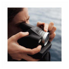 Person holding a black Polaroid I-2 instant camera with a prominent silver lens, looking through the viewfinder.