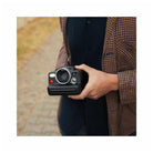 Person holding a black Polaroid I-2 instant camera with a prominent lens and red shutter button outdoors.