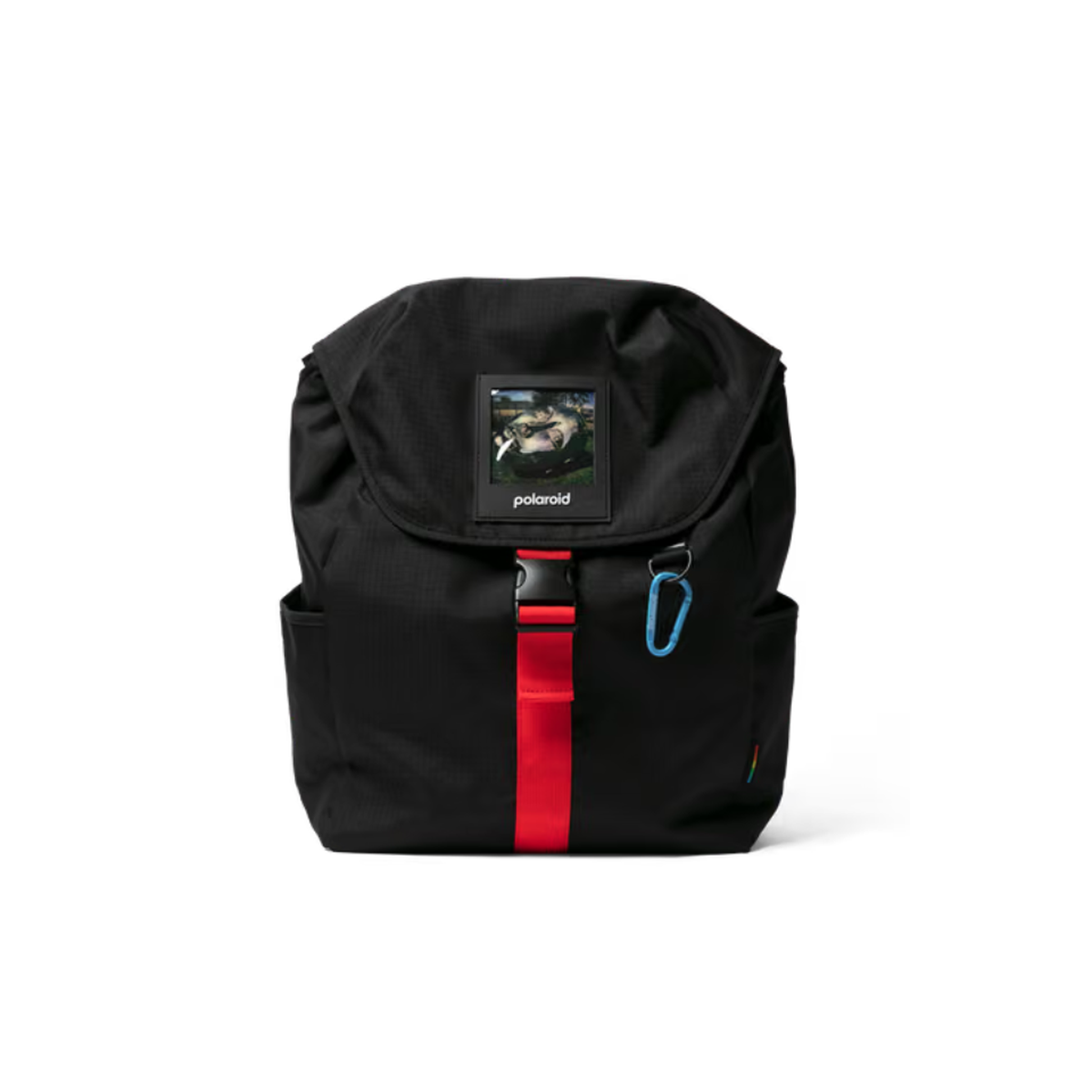 A black Polaroid backpack with a front flap pocket featuring a Polaroid camera patch, a vertical red stripe with a black buckle, and a blue carabiner clip on a white background.