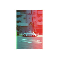 Vintage white VW Beetle parked on a street with red and blue-green holographic light leak effects on the frame edges.