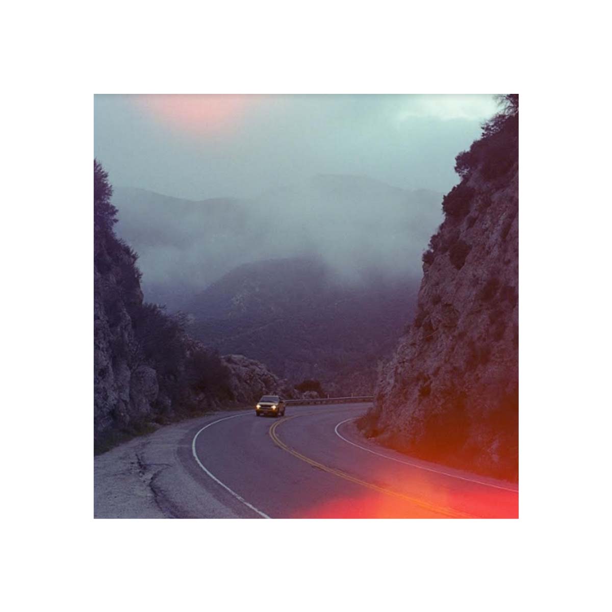 Winding mountain road at dusk with red and purple light leaks from Psychedelic Blues 35mm film.