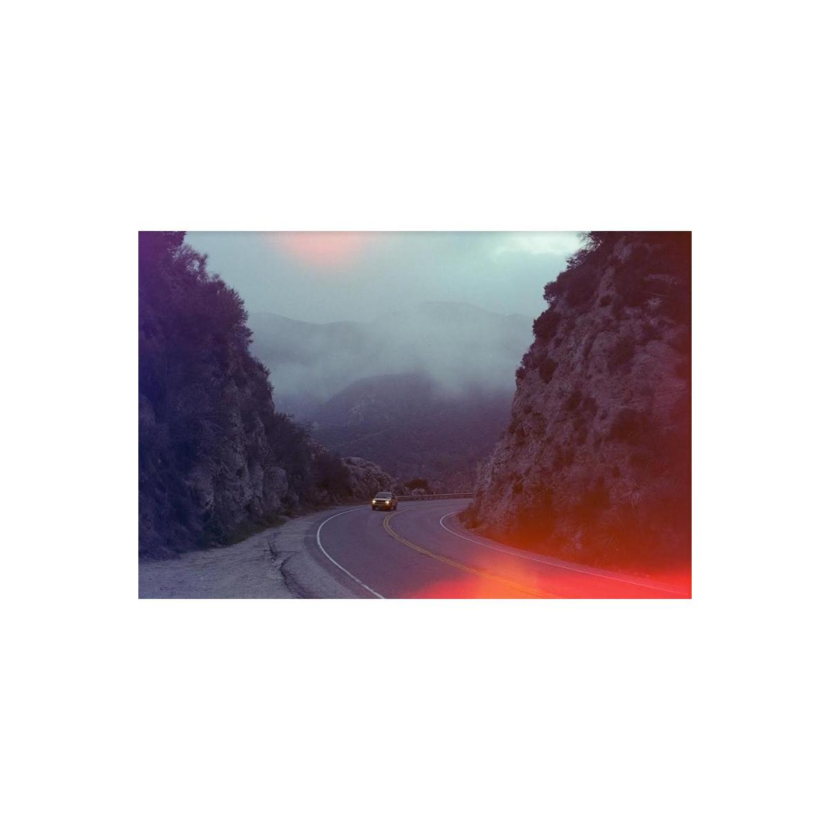 Winding mountain road with a car, featuring vibrant red and purple light-leak effects from Psychedelic Blues 35mm film.