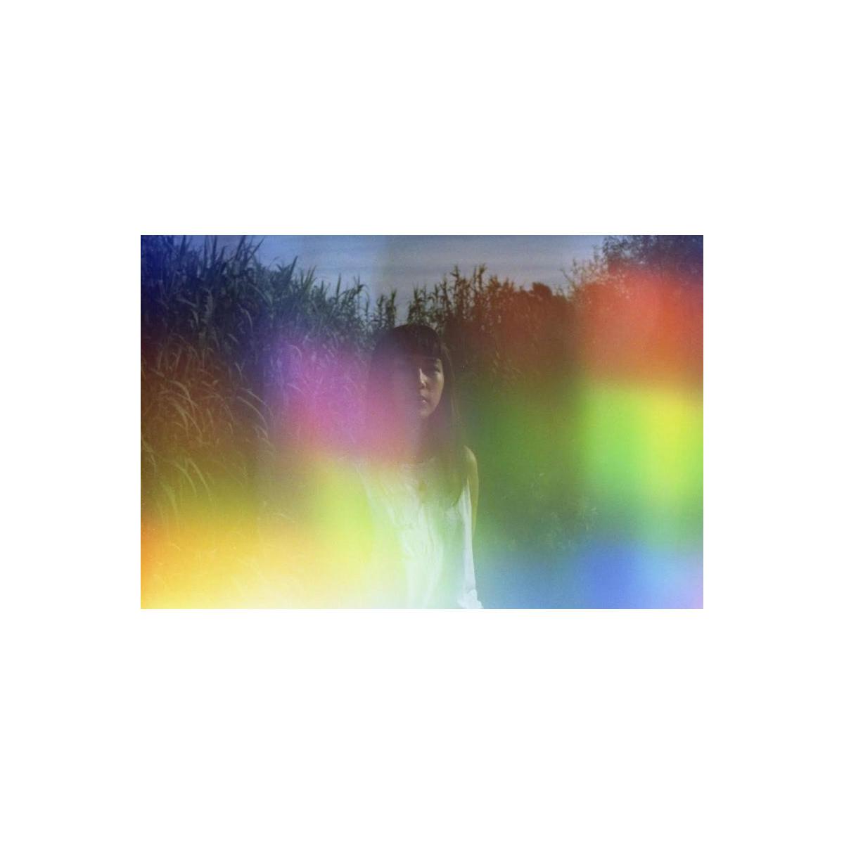 Portrait of a person in tall grass with holographic rainbow light leaks and vibrant color shifts from 35mm film.