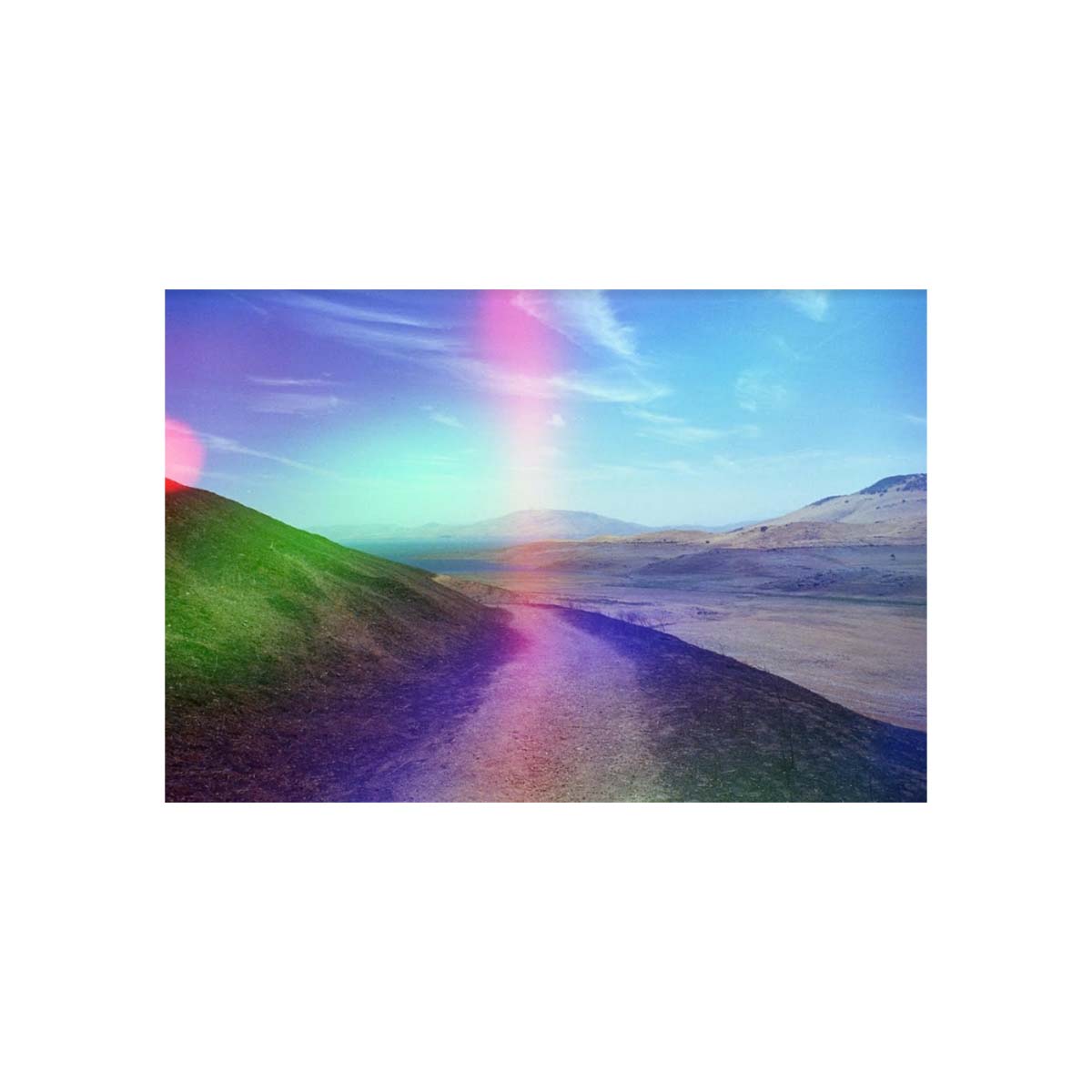 Landscape shot of a dirt path through hills featuring holographic rainbow light leaks from Psychedelic Blues 35mm film.