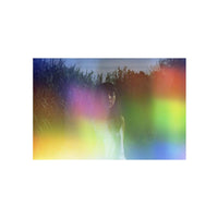 Portrait of a woman in tall grass, overlaid with vibrant, holographic rainbow light leaks from Psychedelic Blues 35mm film.