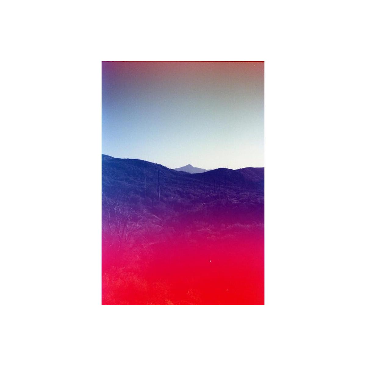 35mm film shot of a mountain landscape featuring a vibrant red light leak and blue color wash across the frame.