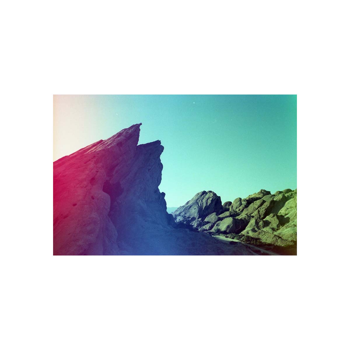 Rocky landscape captured on 35mm film with vibrant red light leaks and teal color shifts across the sky.