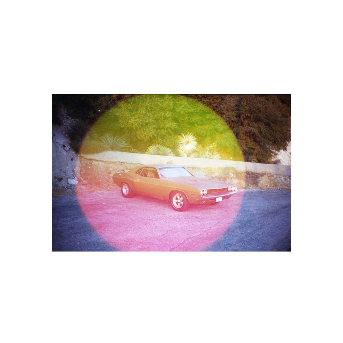 Vintage car parked on asphalt with a large, circular pink and yellow light leak effect from Psychedelic Blues 35mm film.