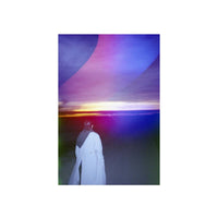 Person in a white coat standing before a sunset with Psychedelic Blues #7 multi-colored wave light-leak effects.