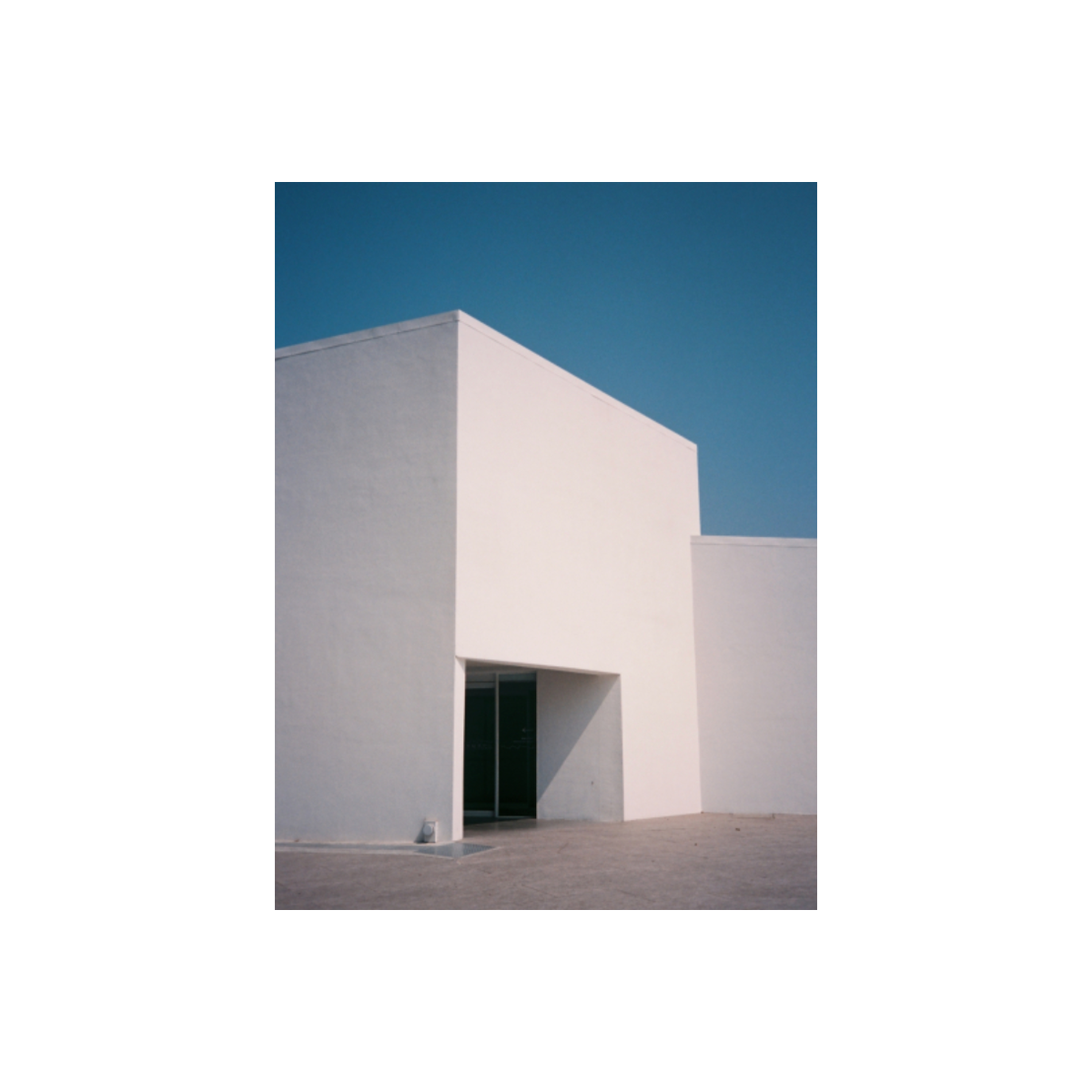 Minimalist white building under a deep cyan sky, captured on RetoColor Maple 100 35mm film with cool blue-green tones.