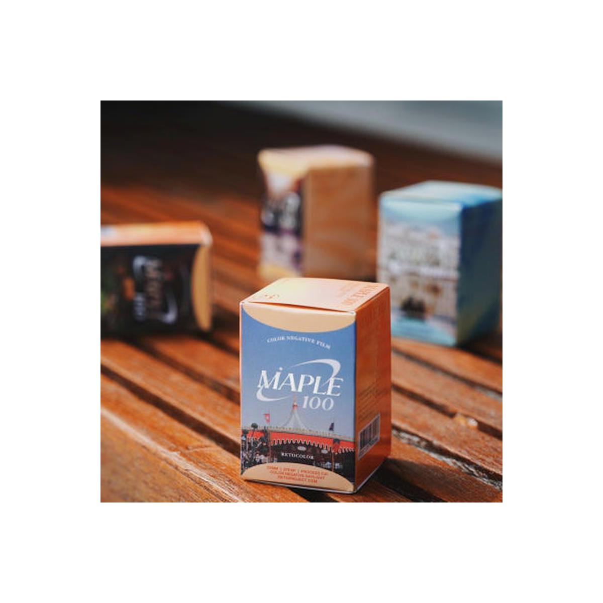 A boxed film canister labeled MAPLE 100 stands on a wooden table, with other blurred boxes in the background.