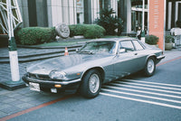 A silver Jaguar S-Type coupe parked on a city street in front of a modern building, with a Japanese license plate visible.