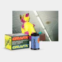 A GRAFX 35mm graphic overlay film box and a single roll of 'Shattered' series film displayed in front of a sample preview image showing a yellow and purple shredded piñata mask against a cracked ceiling background.