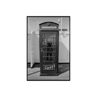 A black and white photograph of a classic British telephone booth, with a reflection of a person visible in the glass door. The words 'TELEPHONE' are printed on the top sign.
