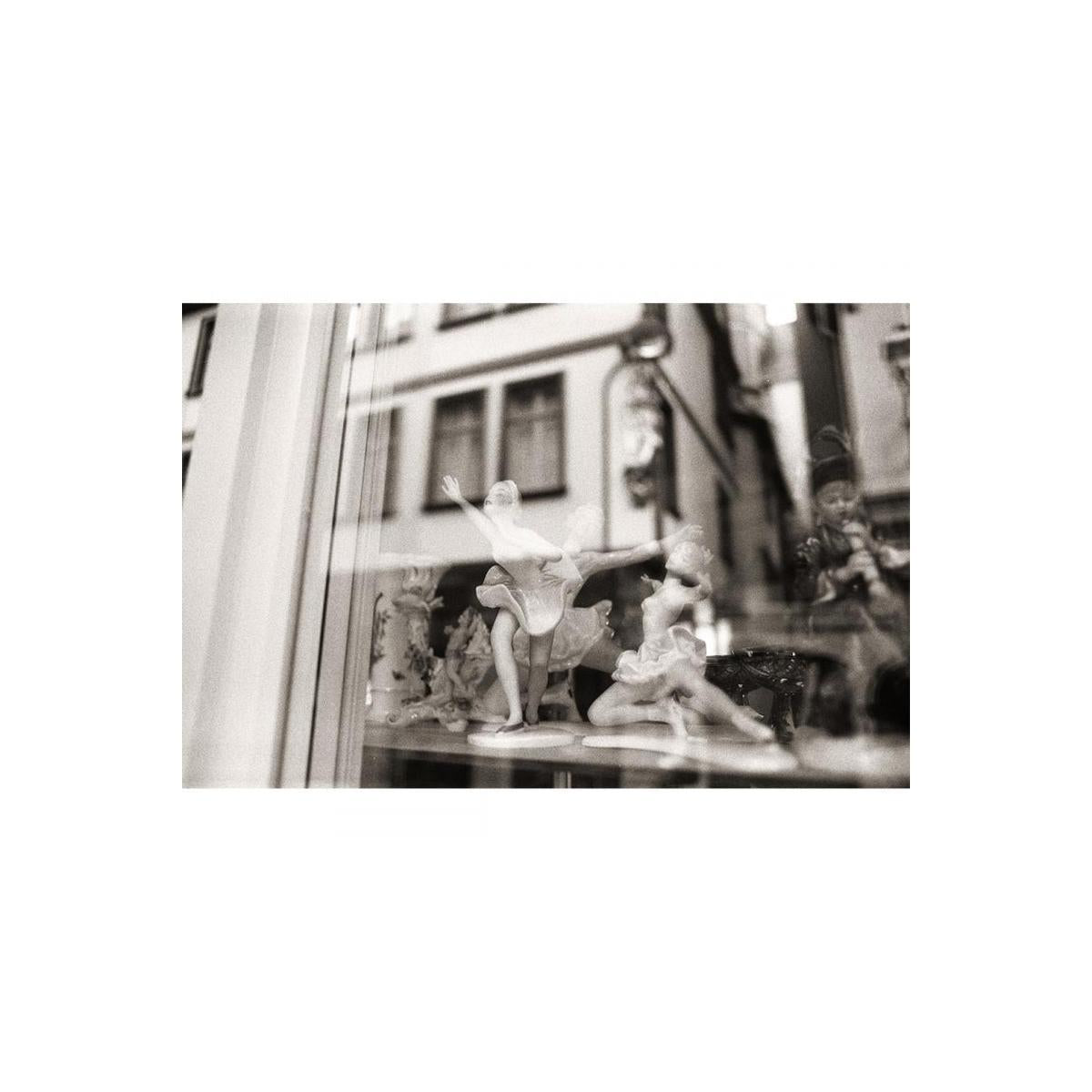 Black and white street photography shot through a window featuring porcelain ballerina figurines.