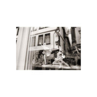 Black and white street photography shot through a window featuring porcelain ballerina figurines.
