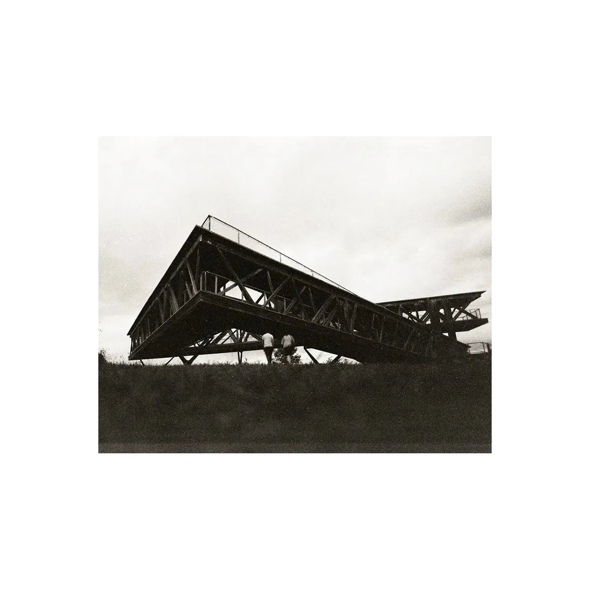 High-contrast black and white street photography of a modern angular metal structure under a cloudy sky.