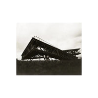 High-contrast black and white street photography of a modern angular metal structure under a cloudy sky.