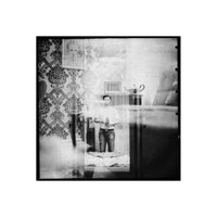 Black and white medium format film shot showing a person reflected in a mirror with vintage wallpaper and high grain.