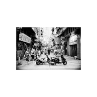 Black and white street scene featuring two parked scooters on a narrow city alleyway with pedestrians and storefronts.