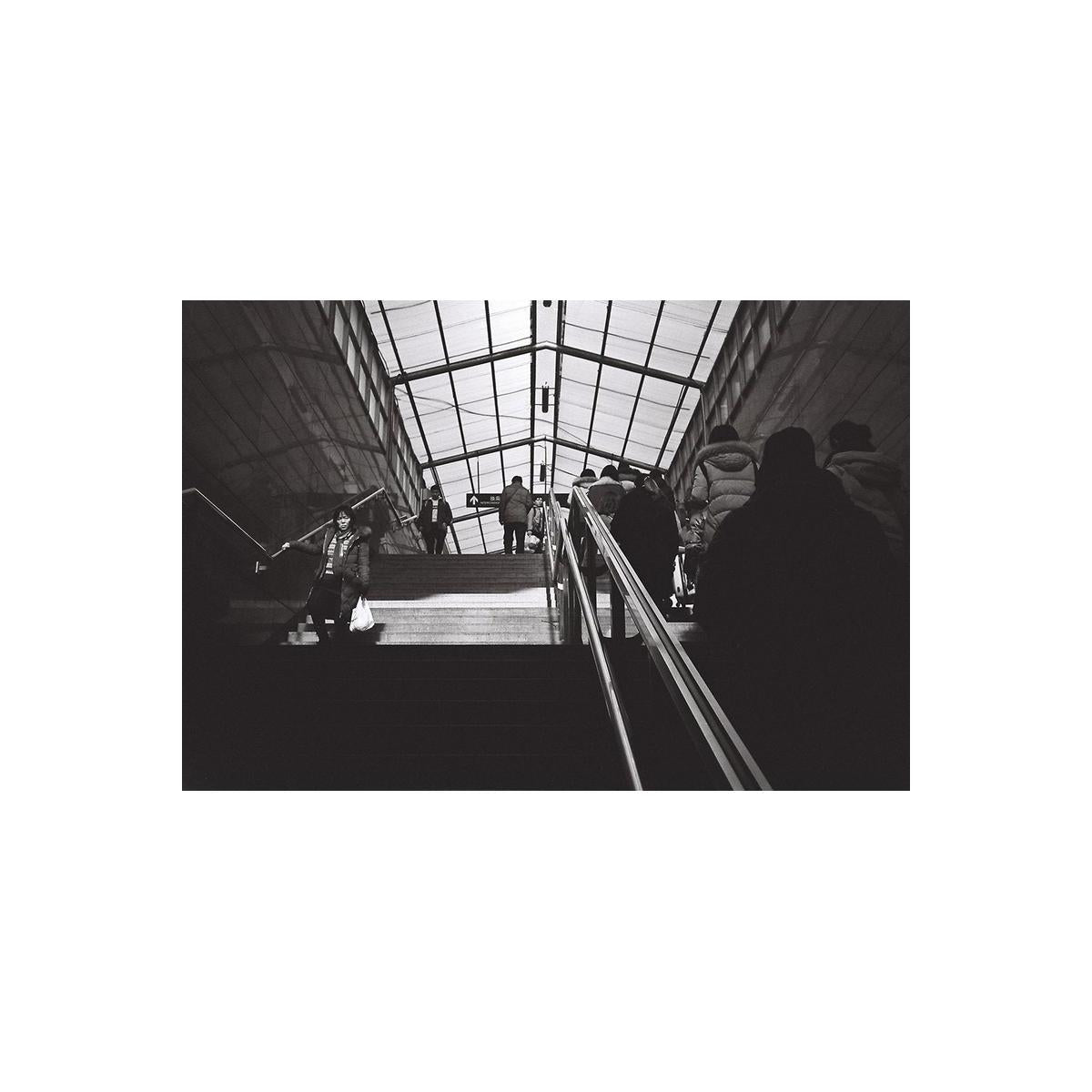 Black and white photo of a person descending stairs in an indoor setting with glass ceiling