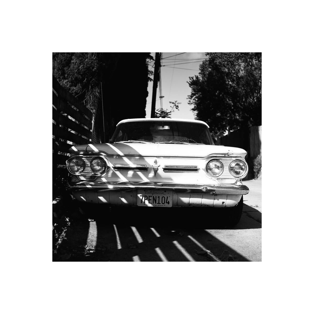 Black and white film shot of a vintage car parked in sunlight, showing high contrast and fine grain detail.