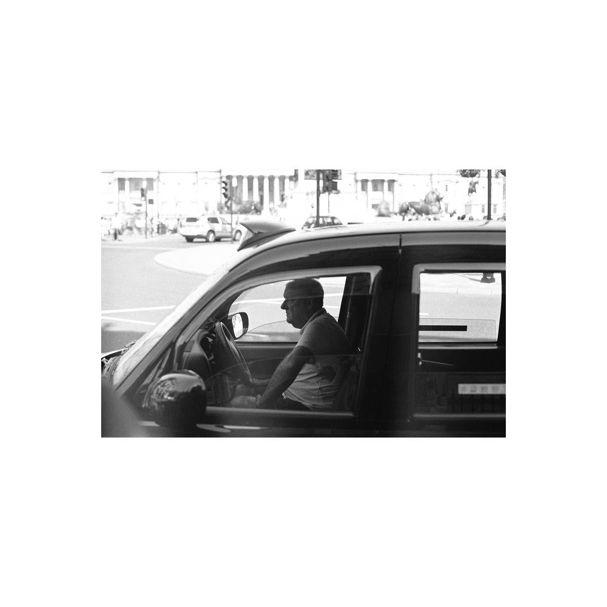 High-contrast black and white street photography shot of a taxi driver in a car, captured on Rollei Superpan 200 film.