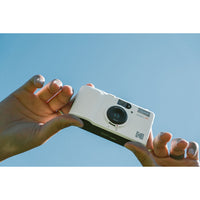Hand holding a white Kodak camera against a clear blue sky