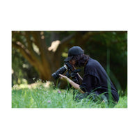 Photographer using a black Sony FE 100mm f/2.8 Macro GM lens to capture close-up shots of wildflowers in a grassy field.