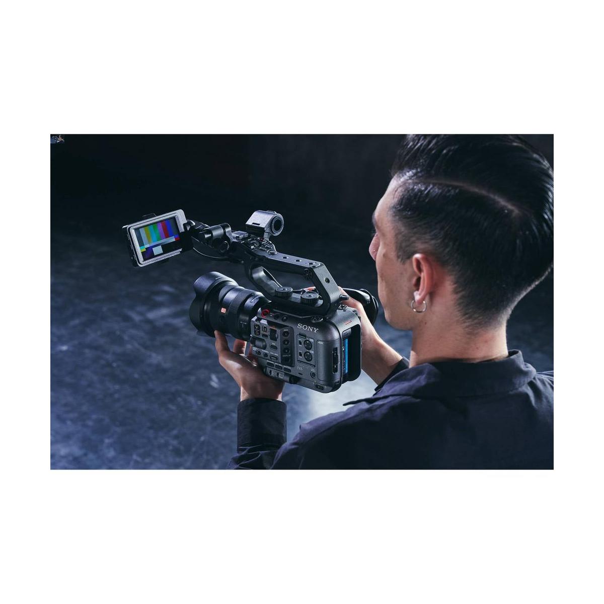 Videographer holding a compact gray Sony FX6 cinema camera with an attached LCD monitor displaying color bars.