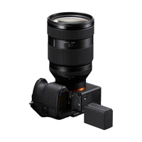 Black Sony NP-SA100 lithium-ion battery placed next to a mirrorless camera with an open battery compartment.