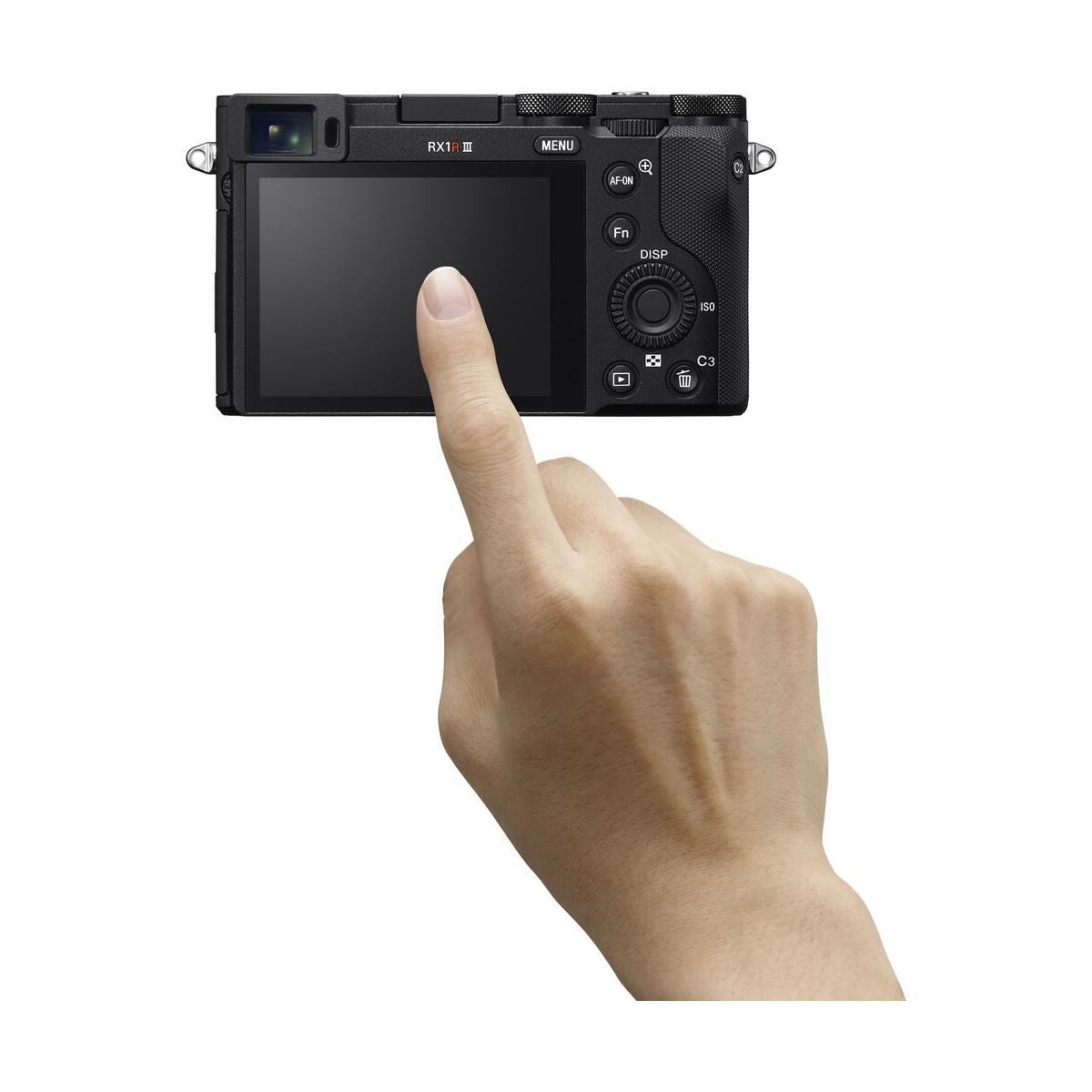 Finger touching the touchscreen LCD of a compact black Sony RX1R III digital camera with rear control buttons.
