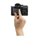 Hand touching the 4-axis touchscreen LCD on the back of a black Sony a7R VI mirrorless camera body.